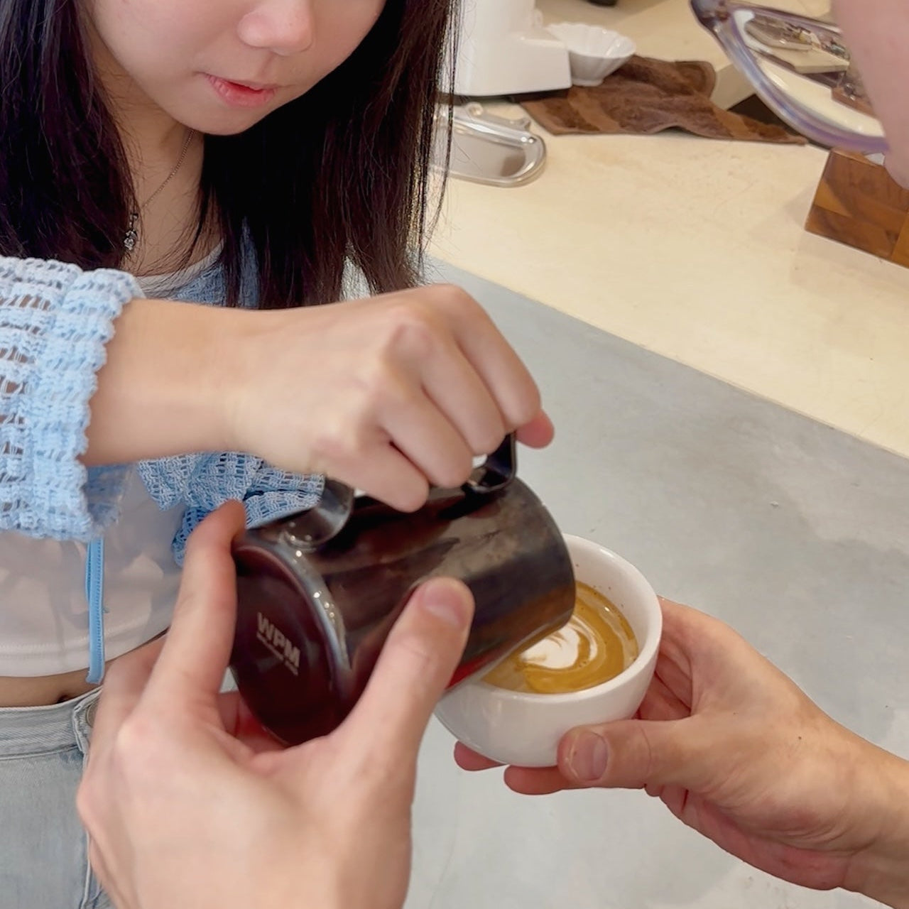 Person pouring a liquid from a small container into a white bowl held by another person.