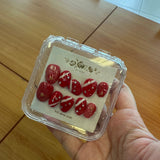 Hand holding a small container with red items on a wooden surface