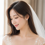 A woman wearing a white lace wedding dress and veil, shown in a close-up portrait with soft indoor lighting and a neutral beige background.