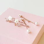 A pair of rose gold floral hair clips with white faux pearls and clear rhinestones, displayed on a textured pink gift box.