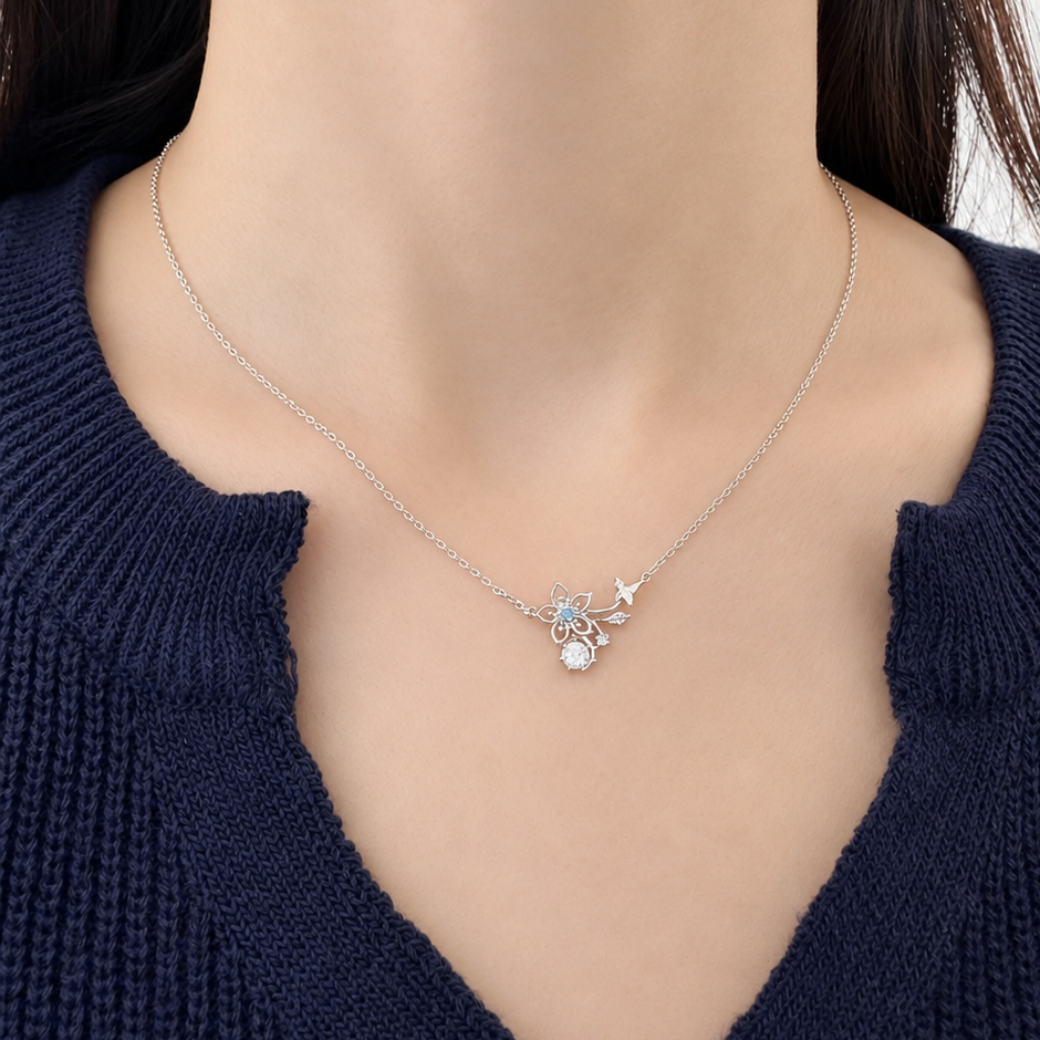 A close-up of a model wearing a delicate silver necklace with a small crystal and star pendant, paired with a dark navy blue knit sweater.