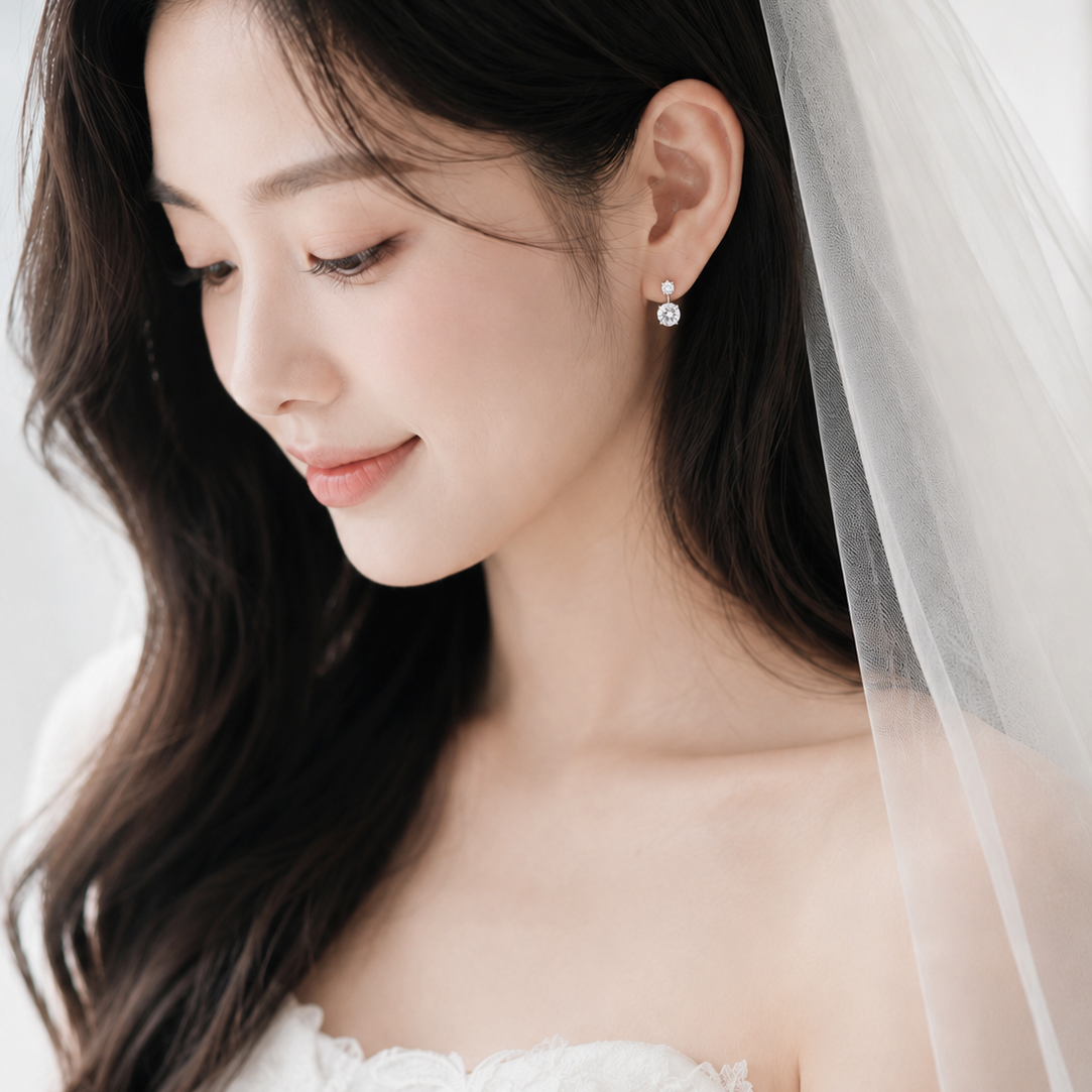 A close-up portrait of a woman wearing a white bridal dress and sheer veil, with a small pearl stud earring visible on one ear.